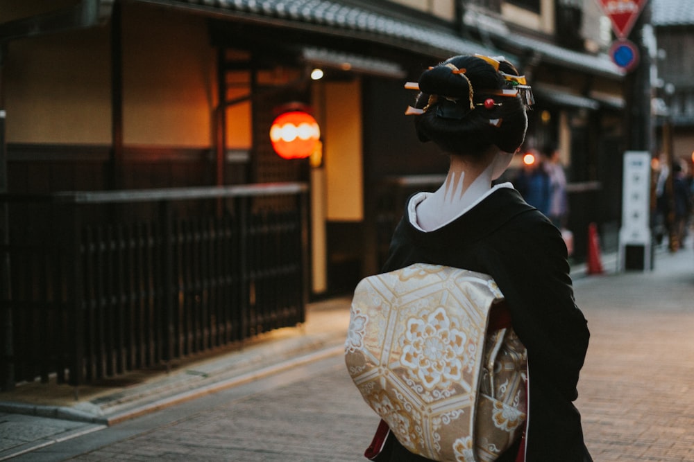 Frau in schwarz-weißem Blumenkimono geht tagsüber auf dem Bürgersteig spazieren