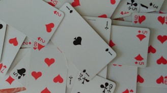 A scattered arrangement of playing cards featuring hearts, clubs, and diamonds. The cards are in a disordered pile, showcasing numbers and suits in red and black colors.