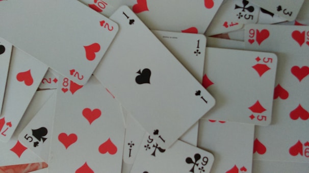 A scattered arrangement of playing cards featuring hearts, clubs, and diamonds. The cards are in a disordered pile, showcasing numbers and suits in red and black colors.