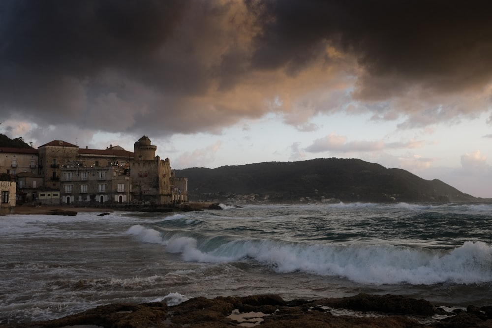 brown concrete building near sea waves under cloudy sky during daytime