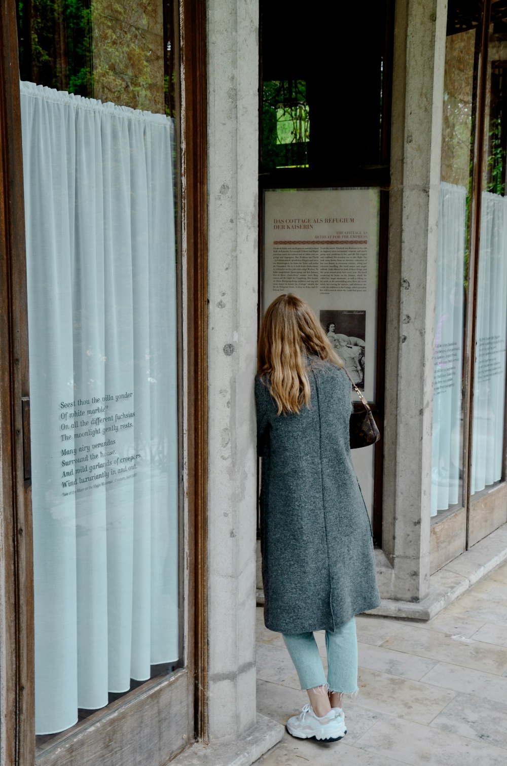 woman in gray coat standing in front of glass window