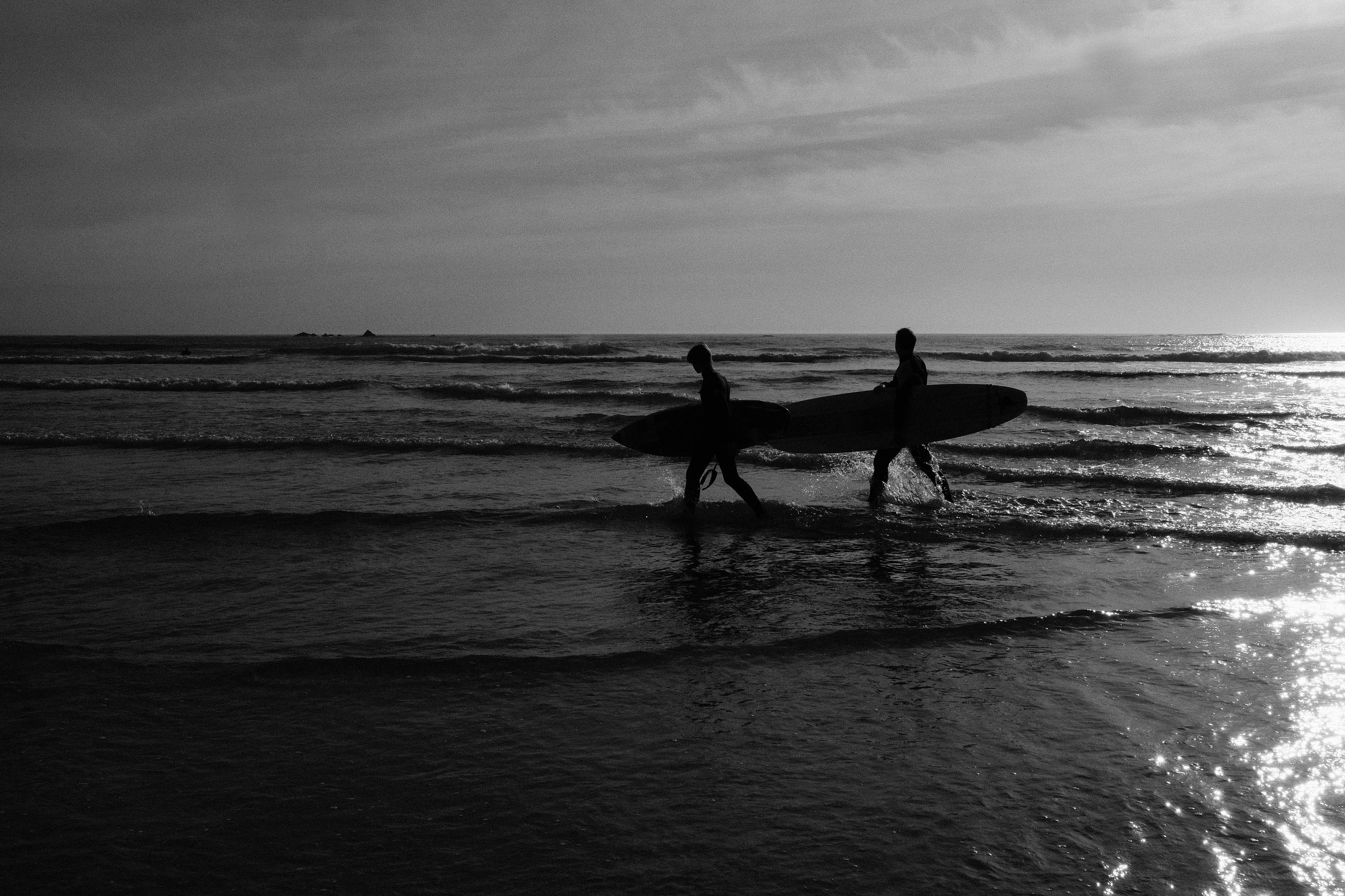 grayscale photo of 2 men and woman holding surfboard on beach