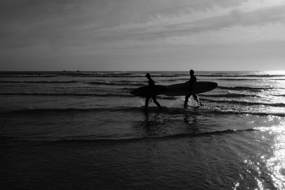 grayscale photo of 2 men and woman holding surfboard on beach