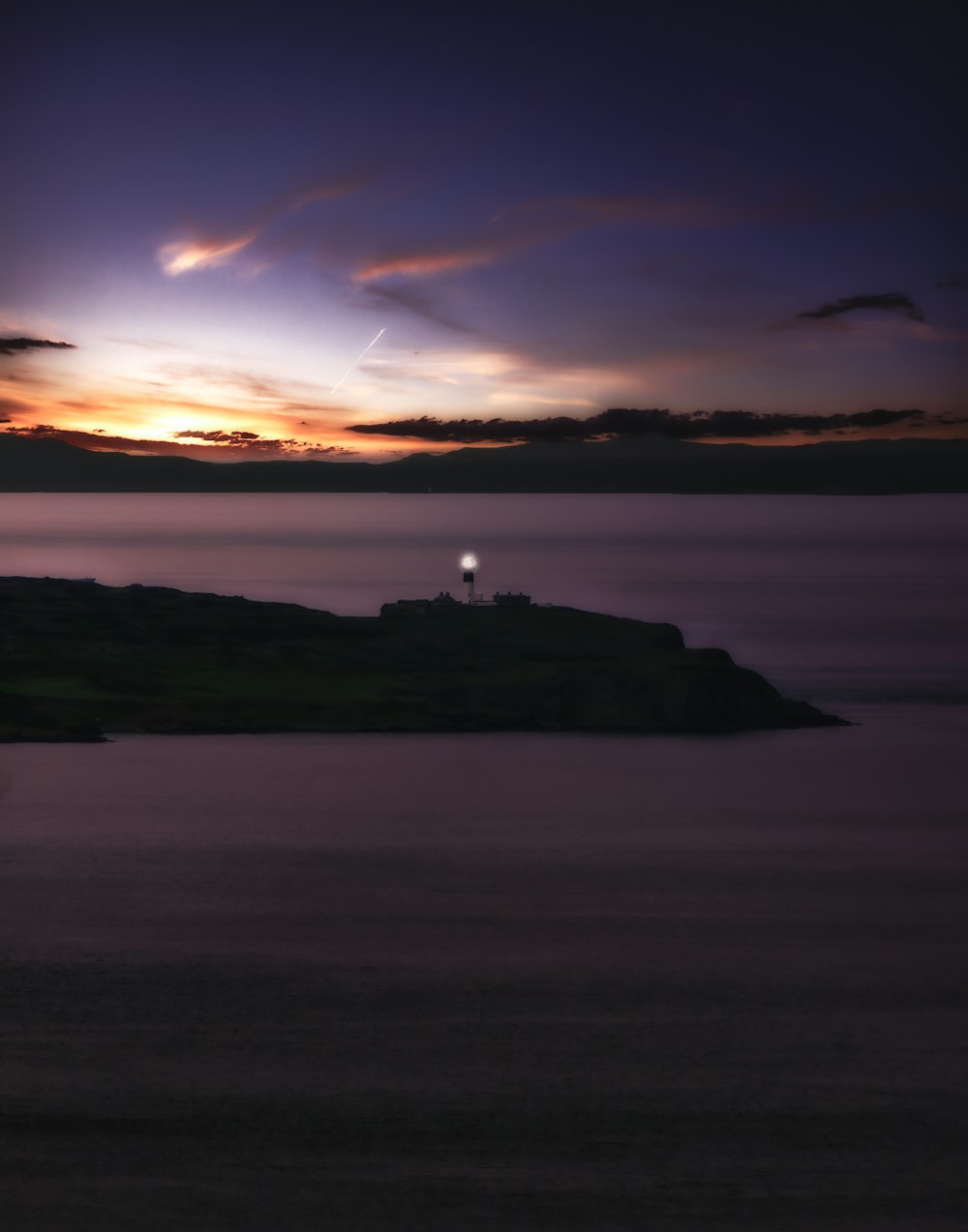 silhouette of person standing on rock formation near body of water during sunset