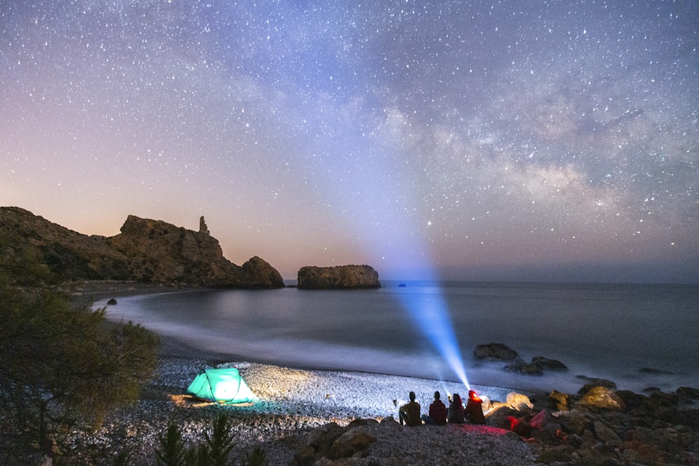 people sitting on rocks near body of water under starry night