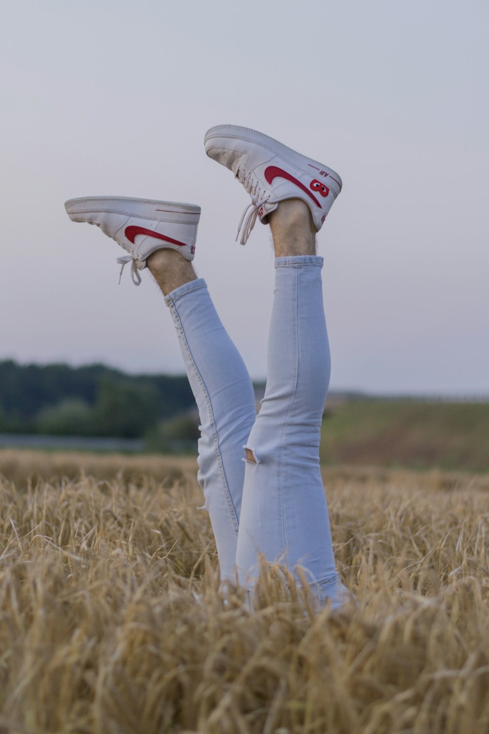 ブルーデニムのジーンズと白とピンクのナイキのスニーカーを履いた人が茶色の芝生の上でジャンプしている
