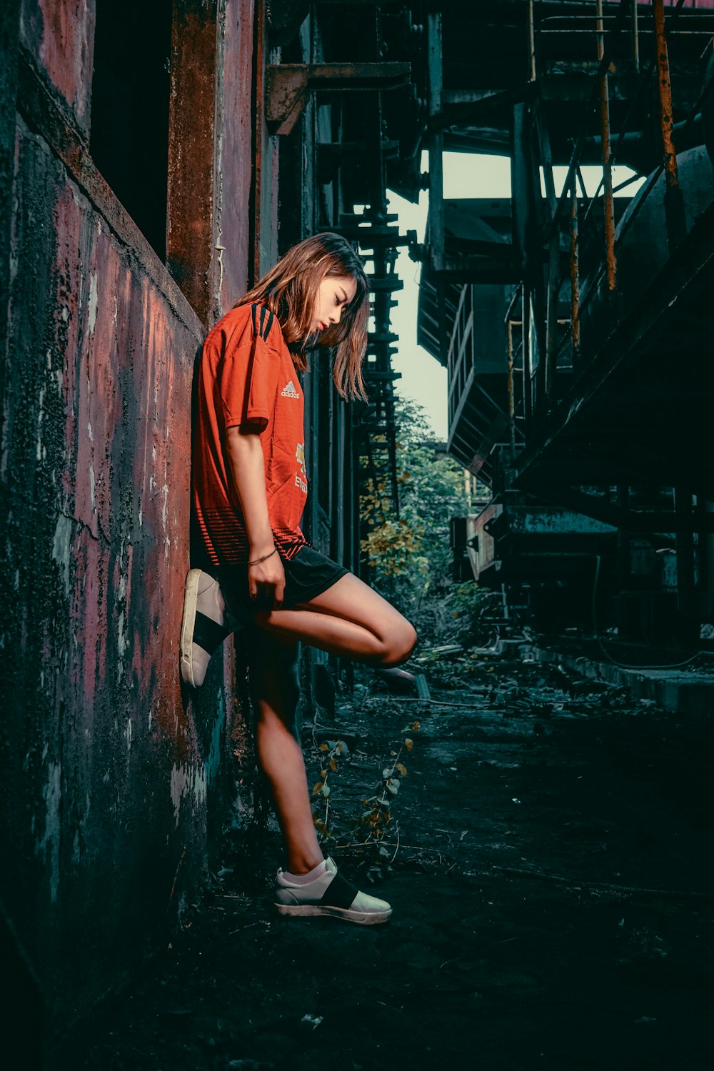 woman in orange jacket and black shorts sitting on brown wooden fence