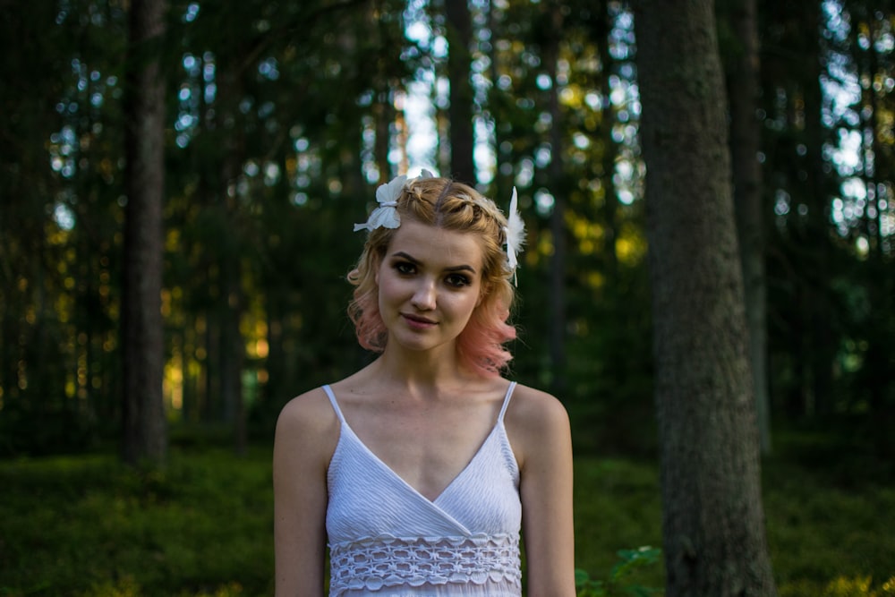 woman in white tank top standing near green trees during daytime