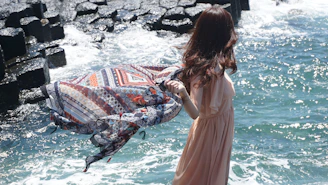 woman in white dress standing on rock near body of water during daytime