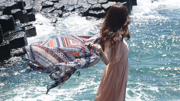 woman in white dress standing on rock near body of water during daytime