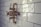 A vintage-style bronze shower valve with white handles is mounted on a glossy white subway-tiled wall. The tiles are rectangular and feature a subtle sheen, accentuating the classic and polished aesthetic of the bathroom fixture.