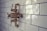 A vintage-style bronze shower valve with white handles is mounted on a glossy white subway-tiled wall. The tiles are rectangular and feature a subtle sheen, accentuating the classic and polished aesthetic of the bathroom fixture.