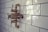 A vintage-style bronze shower valve with white handles is mounted on a glossy white subway-tiled wall. The tiles are rectangular and feature a subtle sheen, accentuating the classic and polished aesthetic of the bathroom fixture.