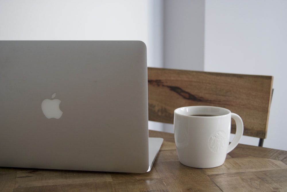 Macbook plateado junto a taza de cerámica blanca sobre mesa de madera marrón