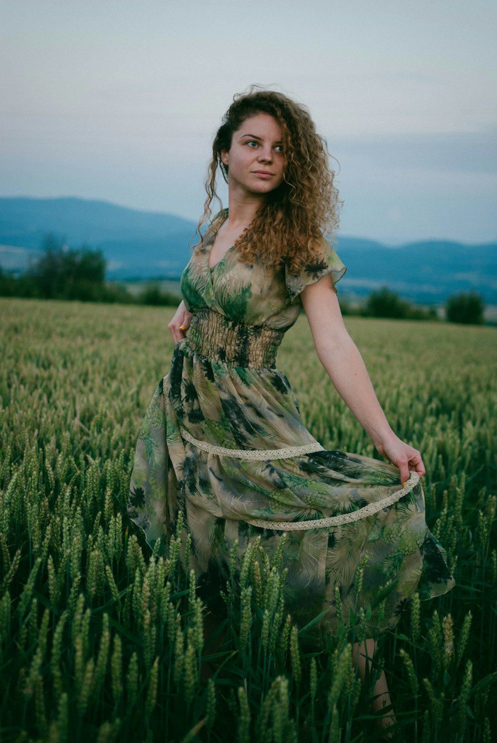 낮 동안 푸른 잔디밭에 서 있는 녹색과 갈색 꽃 드레스를 입은 여자