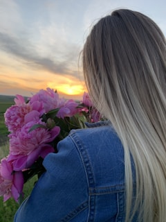 woman in blue denim jacket holding purple flower