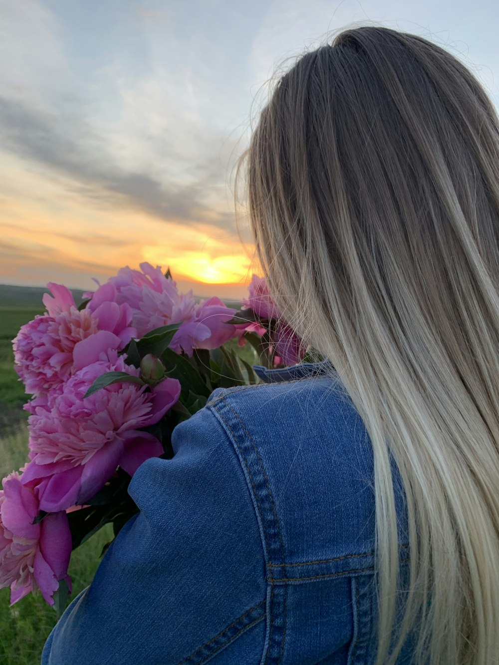 woman in blue denim jacket holding purple flower