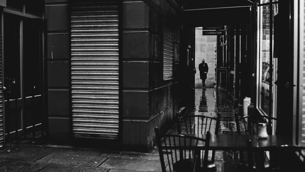 grayscale photo of man walking on sidewalk