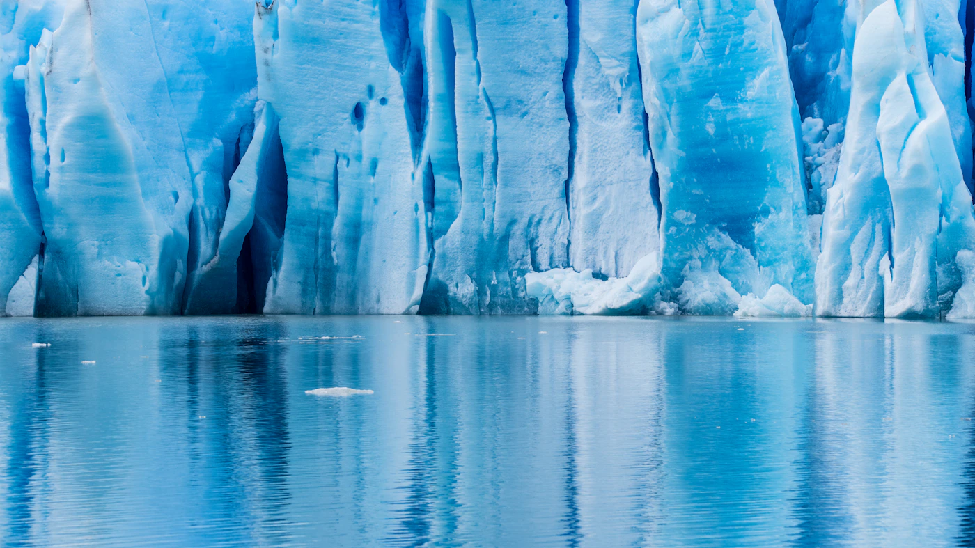 Patagonian glacier with blue ice in the foreground and snowcapped peaks behind under clearing cloud