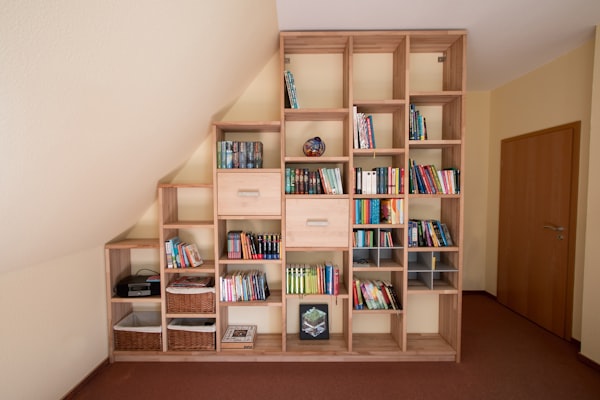 Bespoke fitted timber bookcase built into an under-stairs alcove in a home, with custom shelving shaped to the sloping ceiling