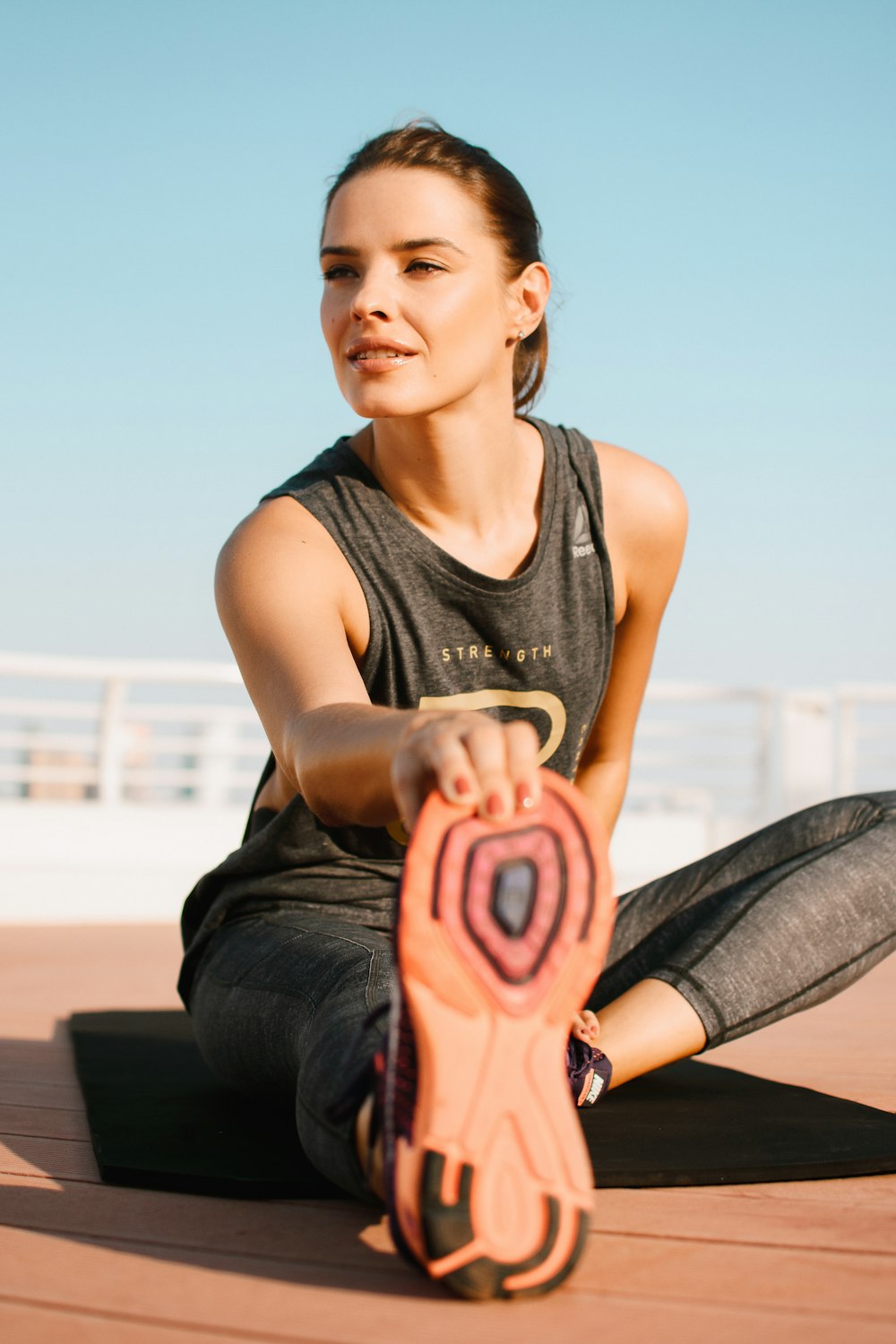 woman in black tank top and blue denim jeans sitting on brown wooden bench during daytime