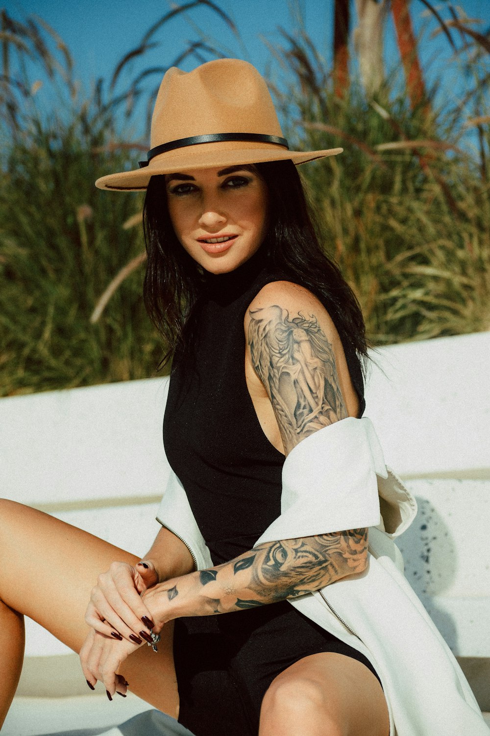 woman in black tank top and white skirt wearing brown hat sitting on white concrete bench