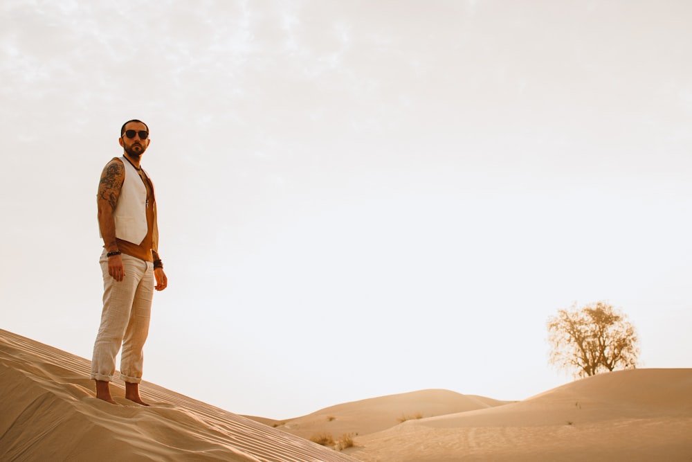 man in white tank top and white pants standing on brown sand during daytime