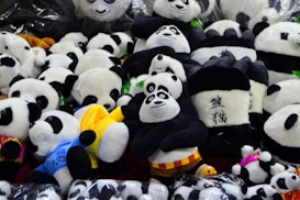 A collection of panda plush toys, some with unique designs and colorful details like blue and yellow clothing. The toys are arranged closely together, creating a playful and cozy atmosphere.