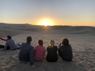 A group of travelers enjoying a peaceful moment watching the sun dip below the desert horizon.
