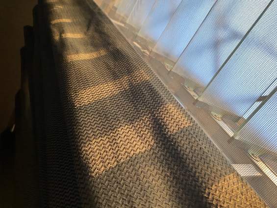 Woven fabric casting shadows with light filtering through a mesh-like surface, creating a pattern of light and shadow in a warm glow.