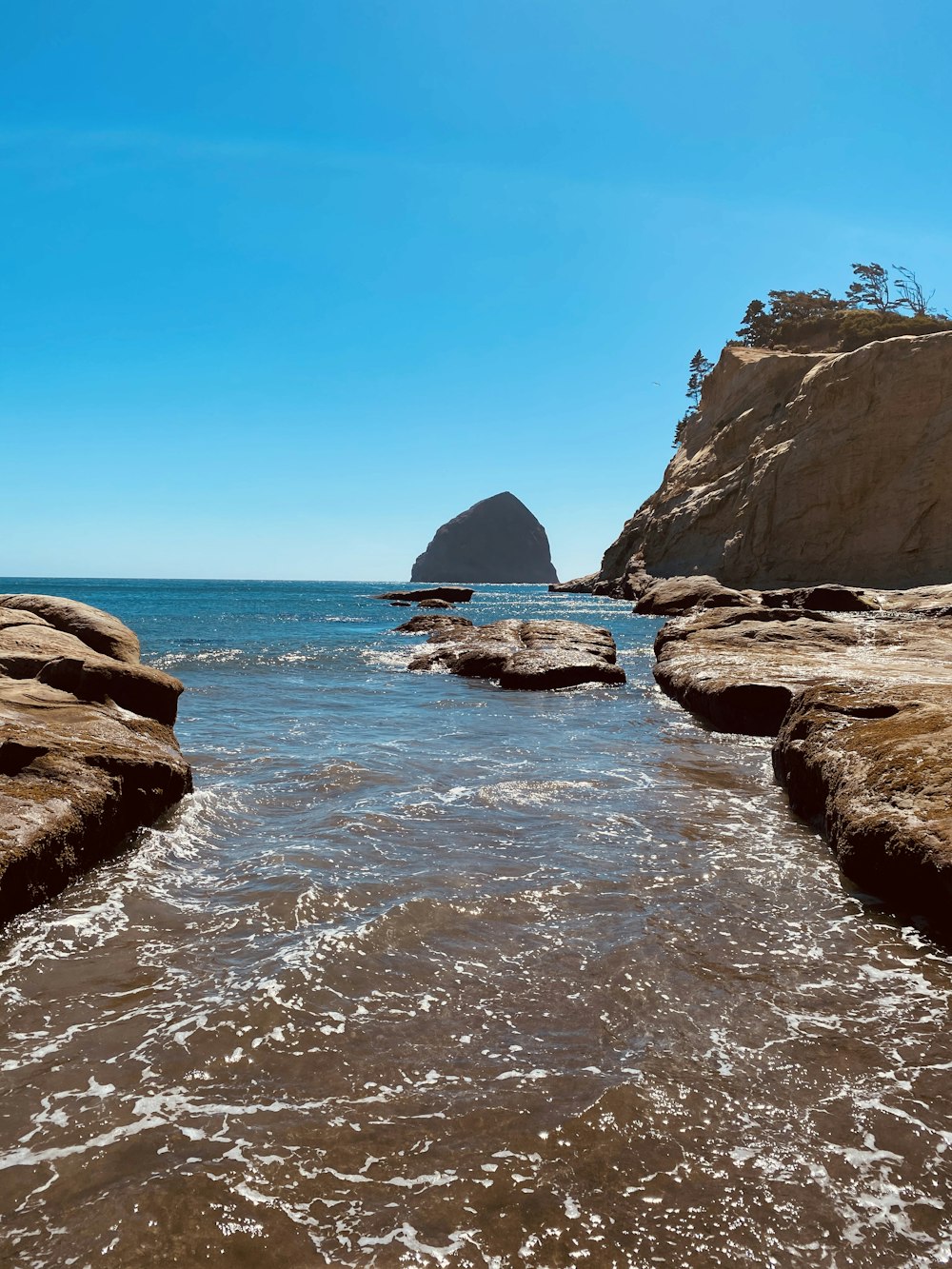 brown rocky mountain beside blue sea under blue sky during daytime