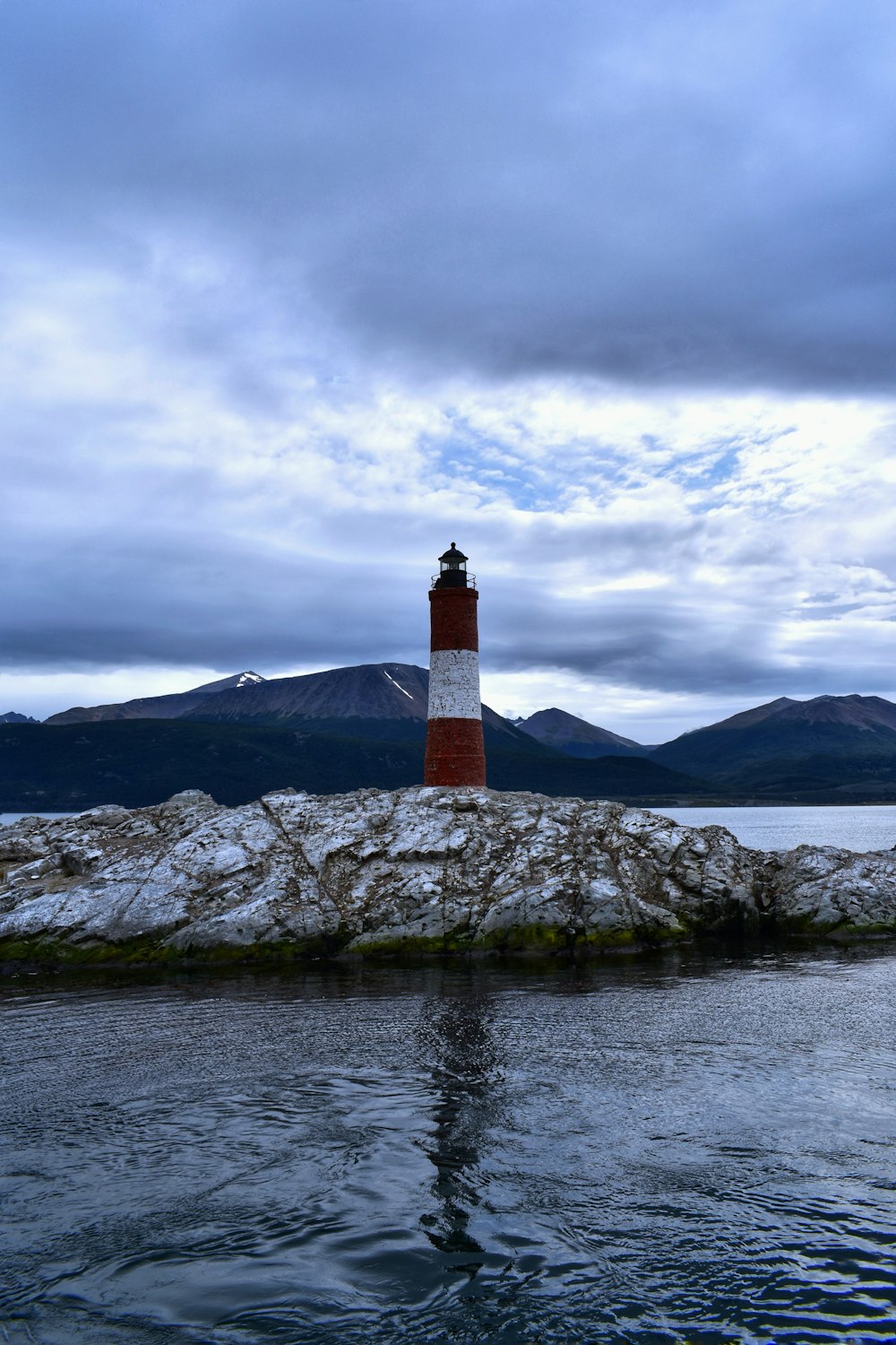 white and red lighthouse on gray rocky mountain under gray cloudy sky during daytime