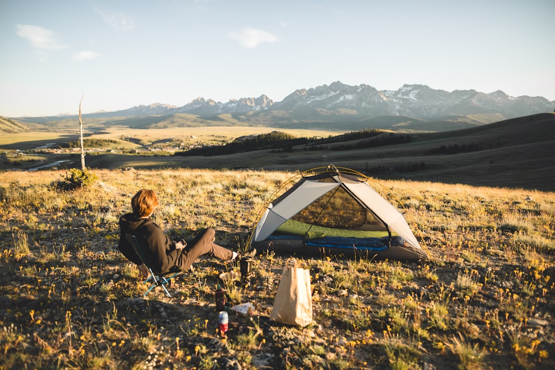 woman in black jacket sitting on green grass field near tent during daytime