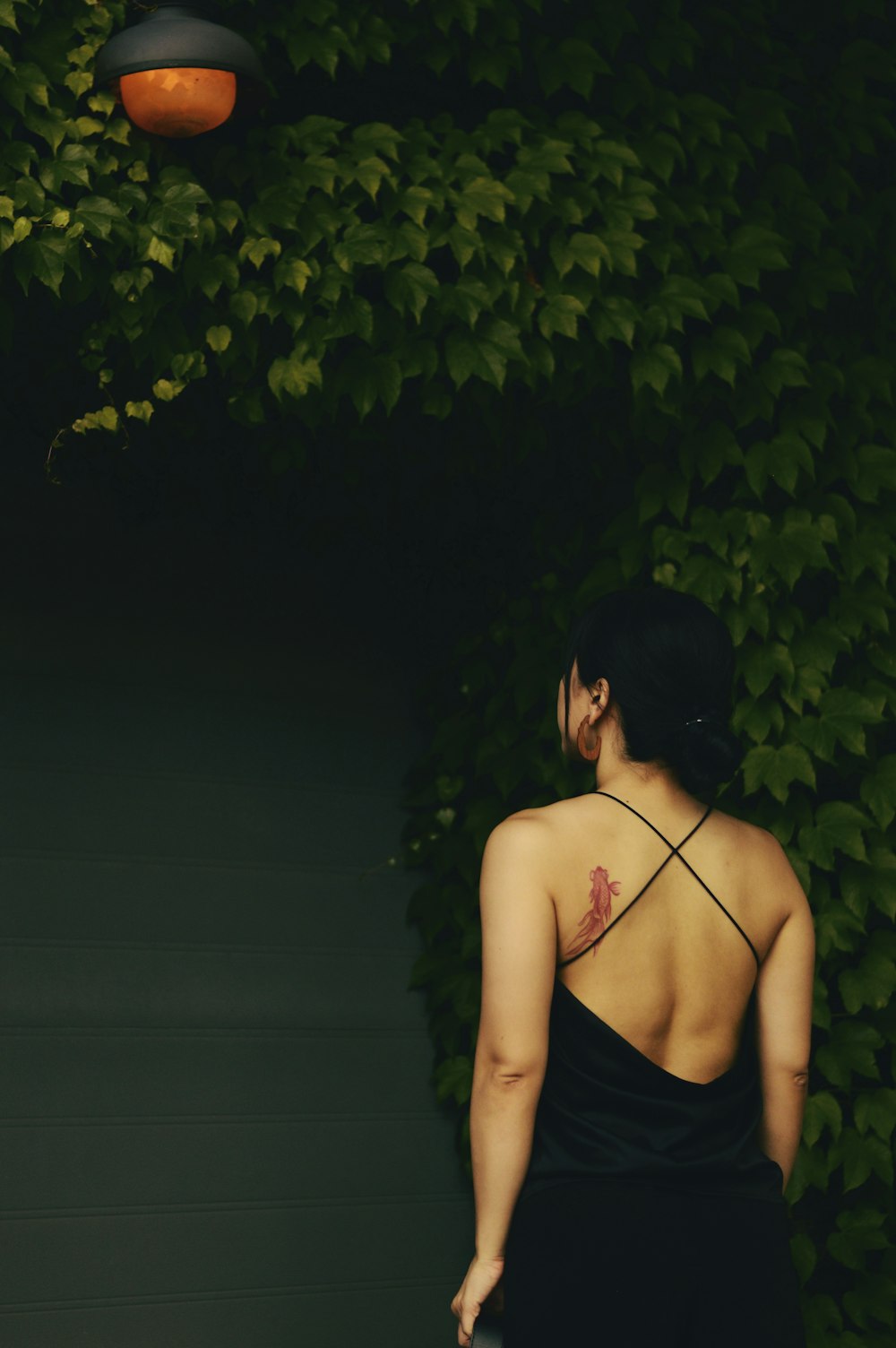 woman in black spaghetti strap top standing in front of black wooden wall