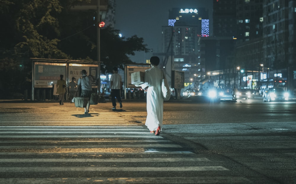 uomo in abito bianco che cammina sulla corsia pedonale durante la notte