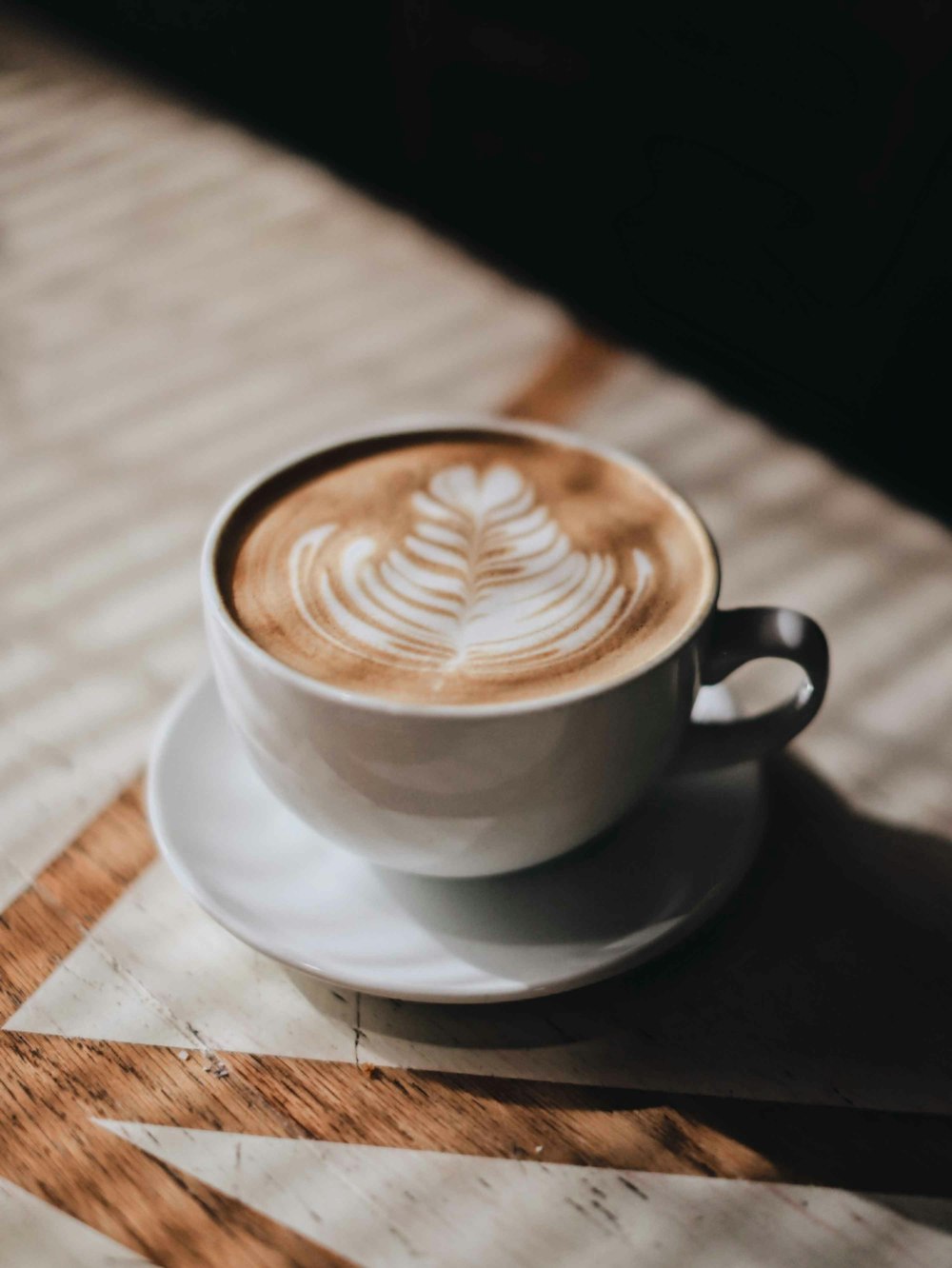 weiße Keramiktasse mit Untertasse auf braunem Holztisch