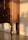 A wooden piece of furniture with intricate carvings and a rich brown finish is bathed in warm sunlight. The shadow of the furniture leg is cast against the cream-colored wall, highlighting the elegant, turned design of the leg.