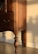 A wooden piece of furniture with intricate carvings and a rich brown finish is bathed in warm sunlight. The shadow of the furniture leg is cast against the cream-colored wall, highlighting the elegant, turned design of the leg.