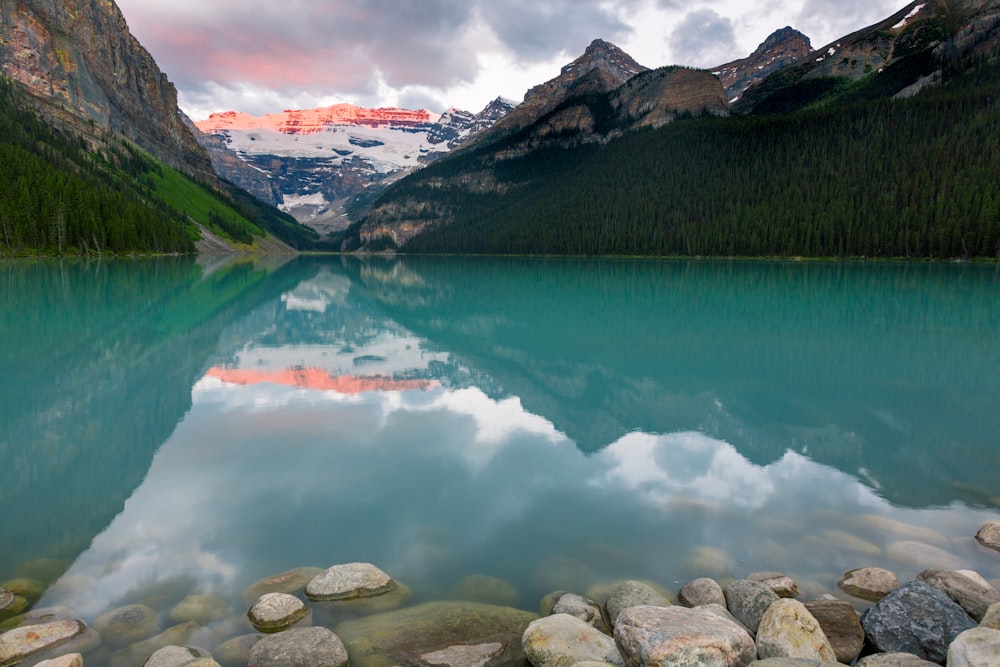 lake near green mountain under white clouds during daytime