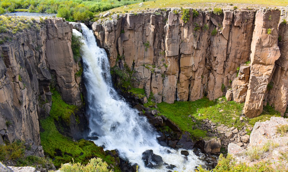 water falls between brown rocky mountain during daytime