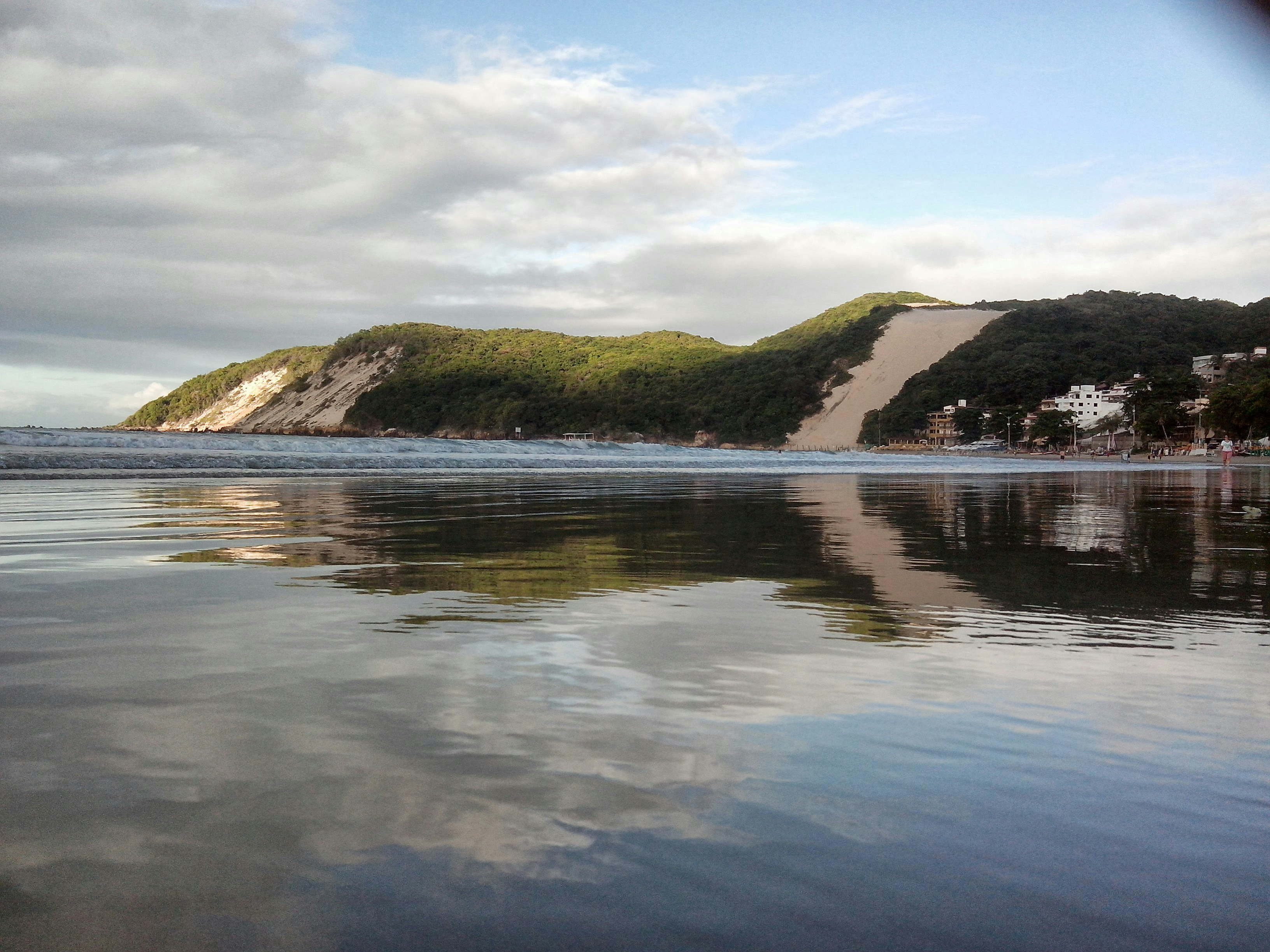 green grass field near body of water under cloudy sky during daytime