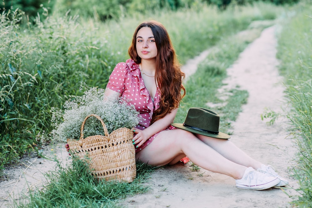 woman in pink and white floral dress sitting on green grass field holding brown woven basket