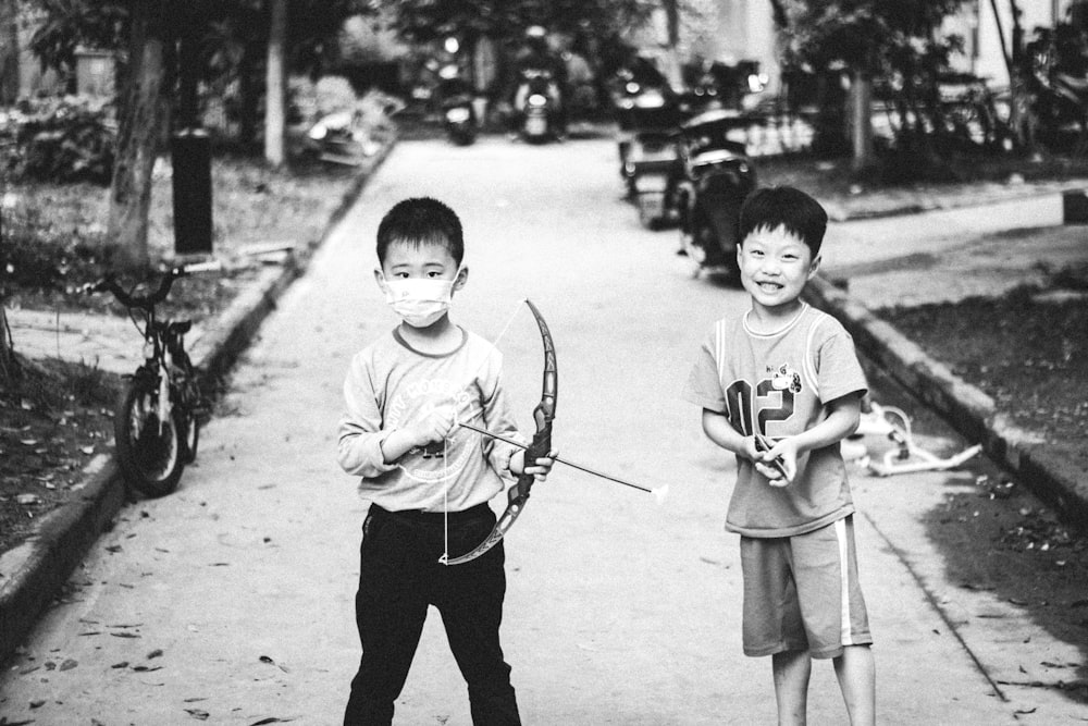 grayscale photo of boy in crew neck t-shirt and black pants holding stick