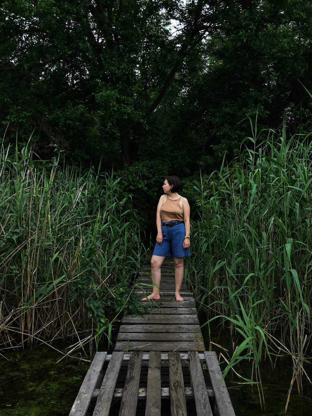 woman in blue tank top and blue denim shorts standing on wooden bridge