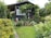 A charming wooden garden shed is surrounded by lush greenery and a variety of colorful flowers. Vines are growing around the structure, and there are decorative elements such as hanging gourds and garden ornaments. The lawn is neatly maintained, and the atmosphere is serene and inviting.