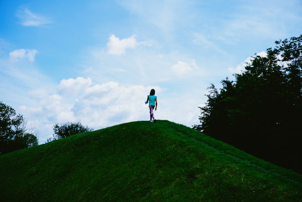 person in black jacket and blue denim jeans walking on green grass field under white clouds