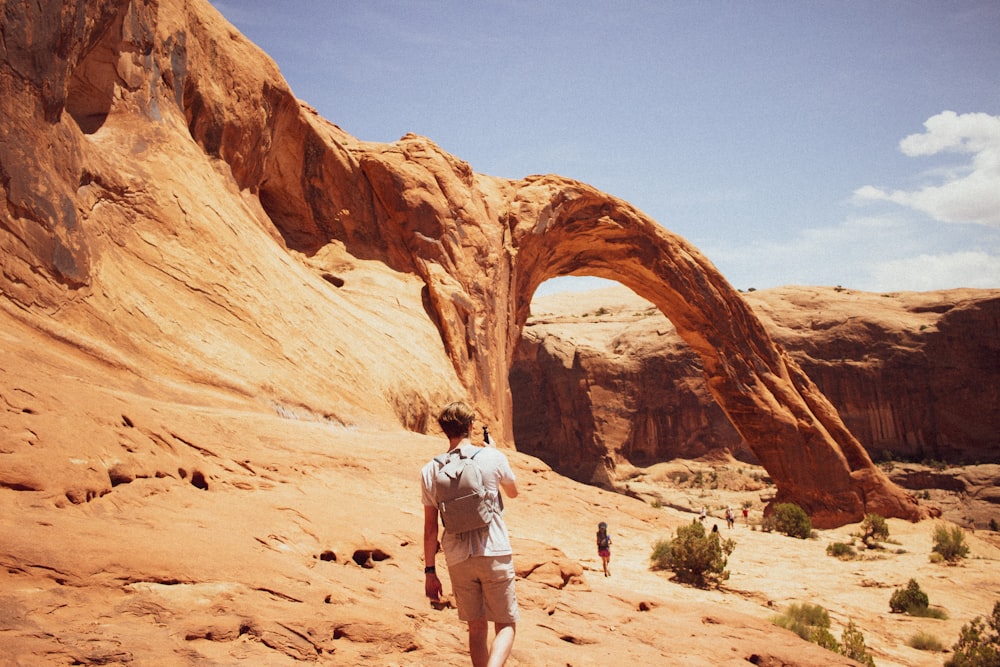 uomo in camicia bianca e pantaloncini bianchi in piedi sulla formazione rocciosa marrone durante il giorno