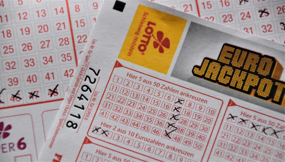 A close-up image of lottery tickets featuring crossed-out numbers, brand logos, and various numbers in a grid format. The tickets have sections for different games, and numbers are marked with black crosses.