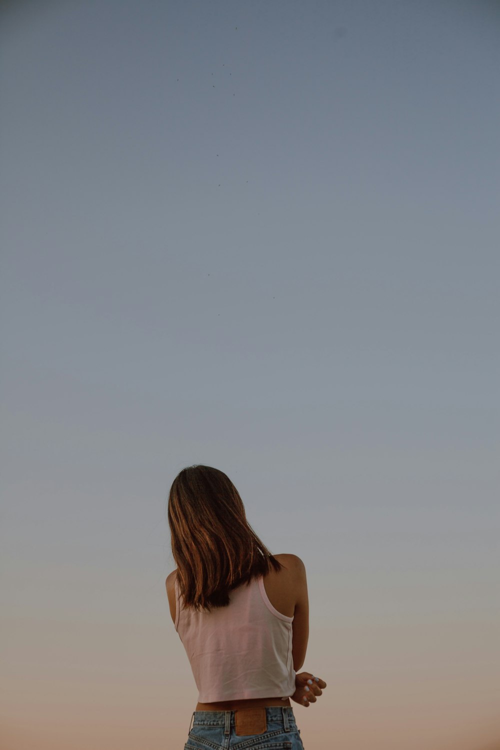 Mujer con camiseta blanca sin mangas mirando al cielo durante el día