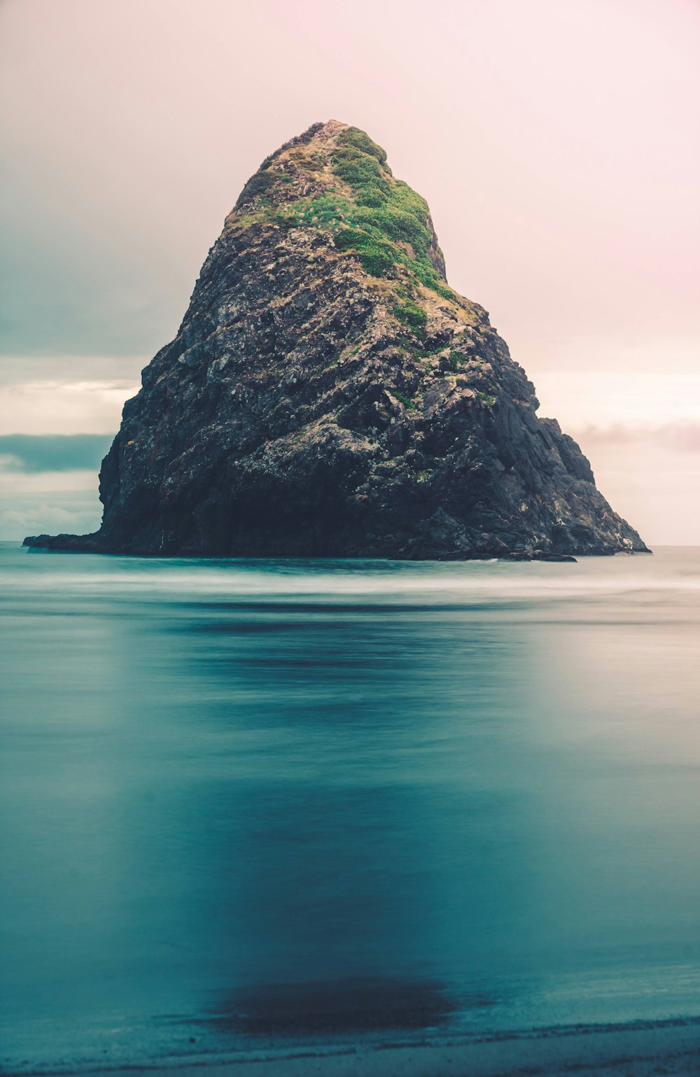 green and black rock formation on blue sea under white sky during daytime